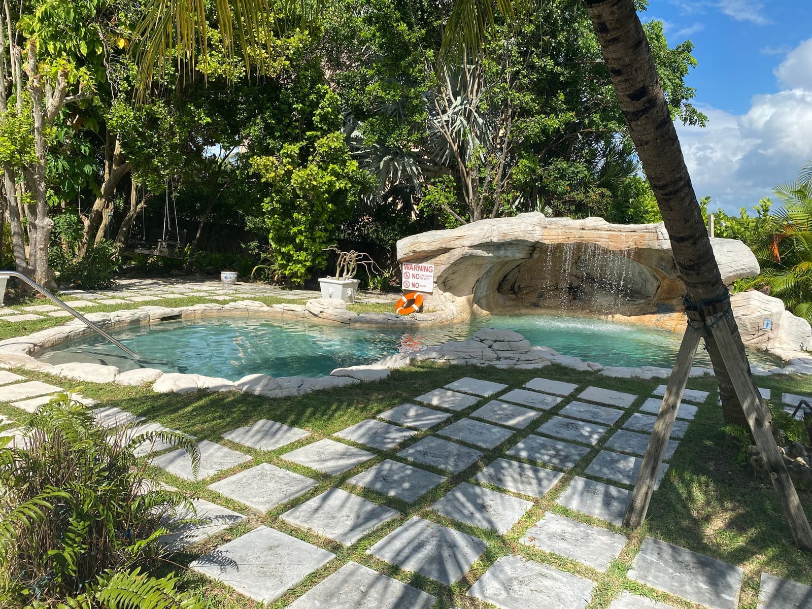 The pool's limestone waterfall, water sliding over pale rock into the shallow end beneath overhanging greenery