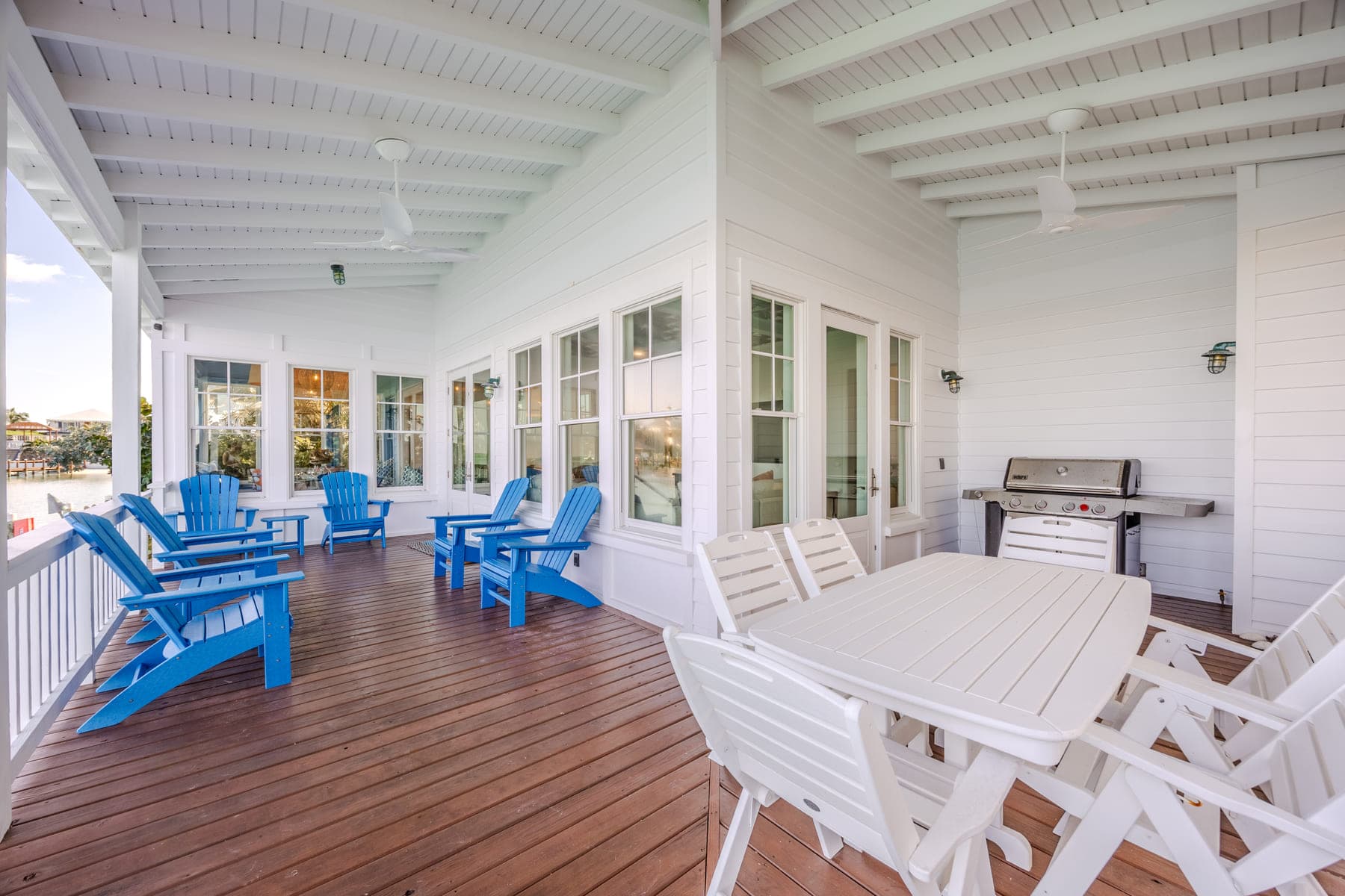 Covered porch with a long outdoor table and Adirondack chairs