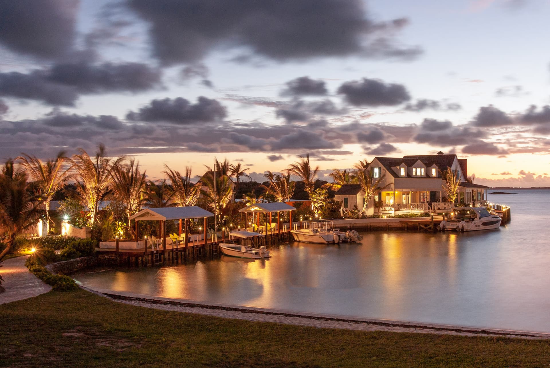 Dusk over the cove at Sunset Point - the dock and its covered slips, moored boats, and a lit clapboard house across the water