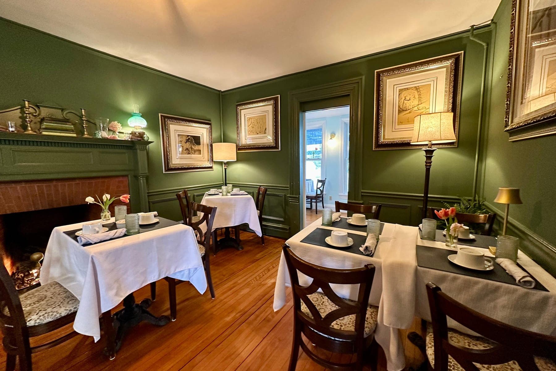 The green dining room with a lit fireplace and three linen-set tables